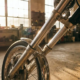 Motorcycle front fork assembly with angled wheel displaying caster geometry, chrome suspension components in garage workshop with golden lighting