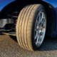 Sports car wheel with negative camber angle showing tilted tire contact patch on asphalt, chrome suspension and coilover springs visible