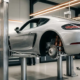 Silver Porsche 718 Cayman on hydraulic lift with rear wheel removed, exposing orange and black Intrax suspension components in modern garage