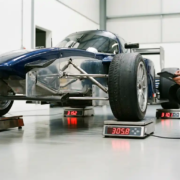 Race car positioned on four digital corner weight scales in professional garage with bright lighting and concrete floors