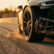 Sports car rear wheel and suspension assembly during high-speed cornering on race track with golden hour lighting