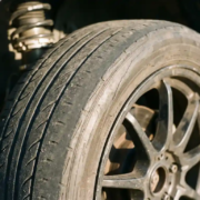 Worn car tire with uneven tread wear on alloy wheel, showing coilover suspension components in background