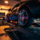 Sports car on professional wheel alignment rack with red laser beams measuring wheels while mechanic adjusts suspension components