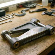 Precision-machined aluminum suspension linkage arm with polished joints on automotive workbench with tools in background