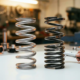 Two automotive coil springs on white workbench showing uniform versus progressive coil spacing designs in metallic silver finish