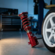 Red anodized coilover suspension assembly mounted on white sports car wheel in professional automotive workshop with dramatic lighting