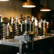 Custom shock absorber on a workshop bench surrounded by competitor suspension components, polished aluminum damper under warm directional lighting.