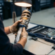 Mechanic's hands inspecting polished Porsche suspension strut on clean workbench with precision tools nearby