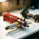 Chrome racing suspension strut with red coil spring on white workbench, standard black component blurred in background