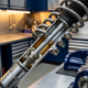 Close-up cross-section of car shock absorber and spring assembly showing piston rod, internal damping chambers, and machined components in automotive workshop