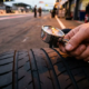 Chrome tire pressure gauge measuring racing tire valve stem with mechanic's gloved hand on blurred pit lane asphalt